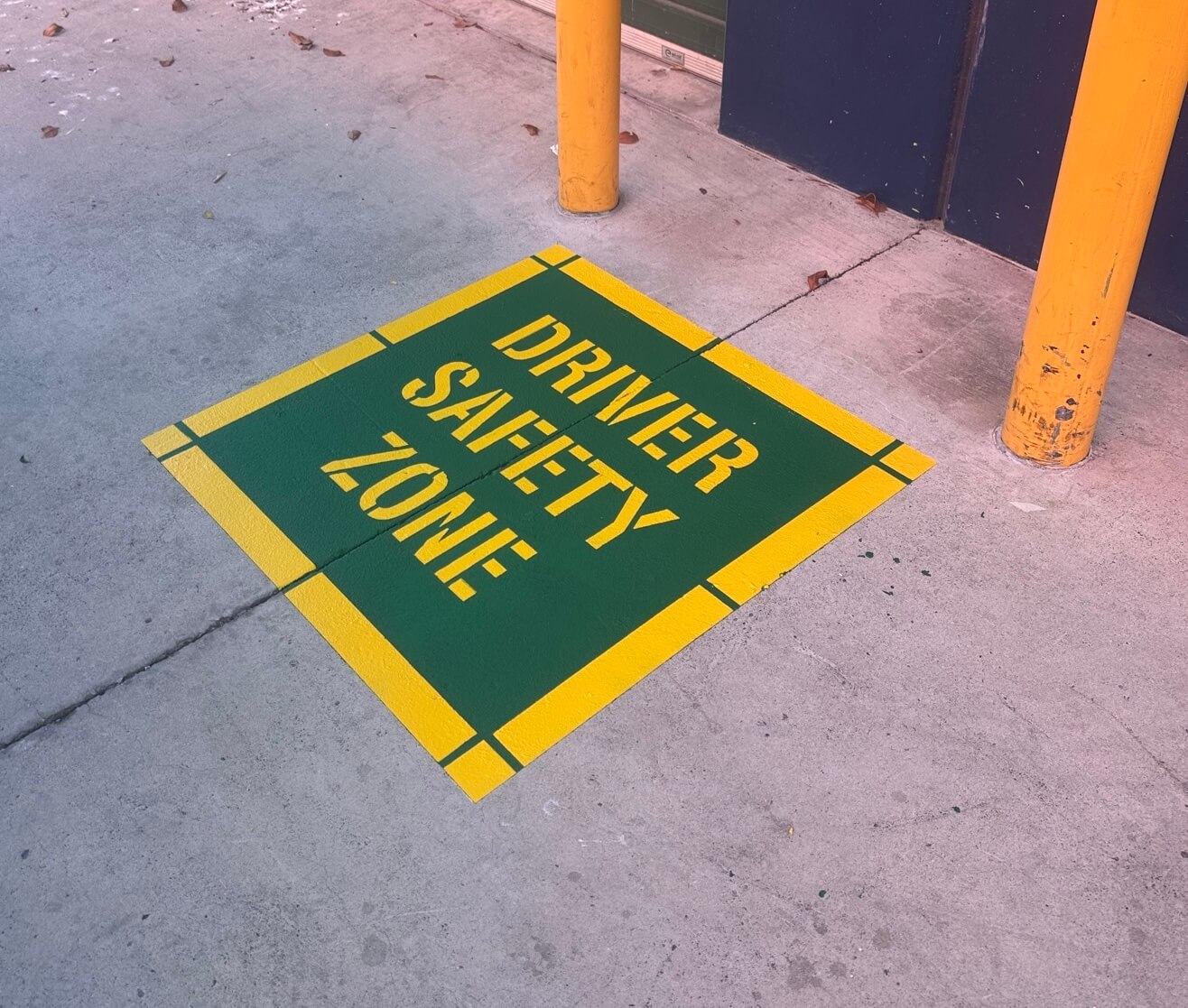 Green and yellow Driver Safety Zone stencil line marking beside bollards