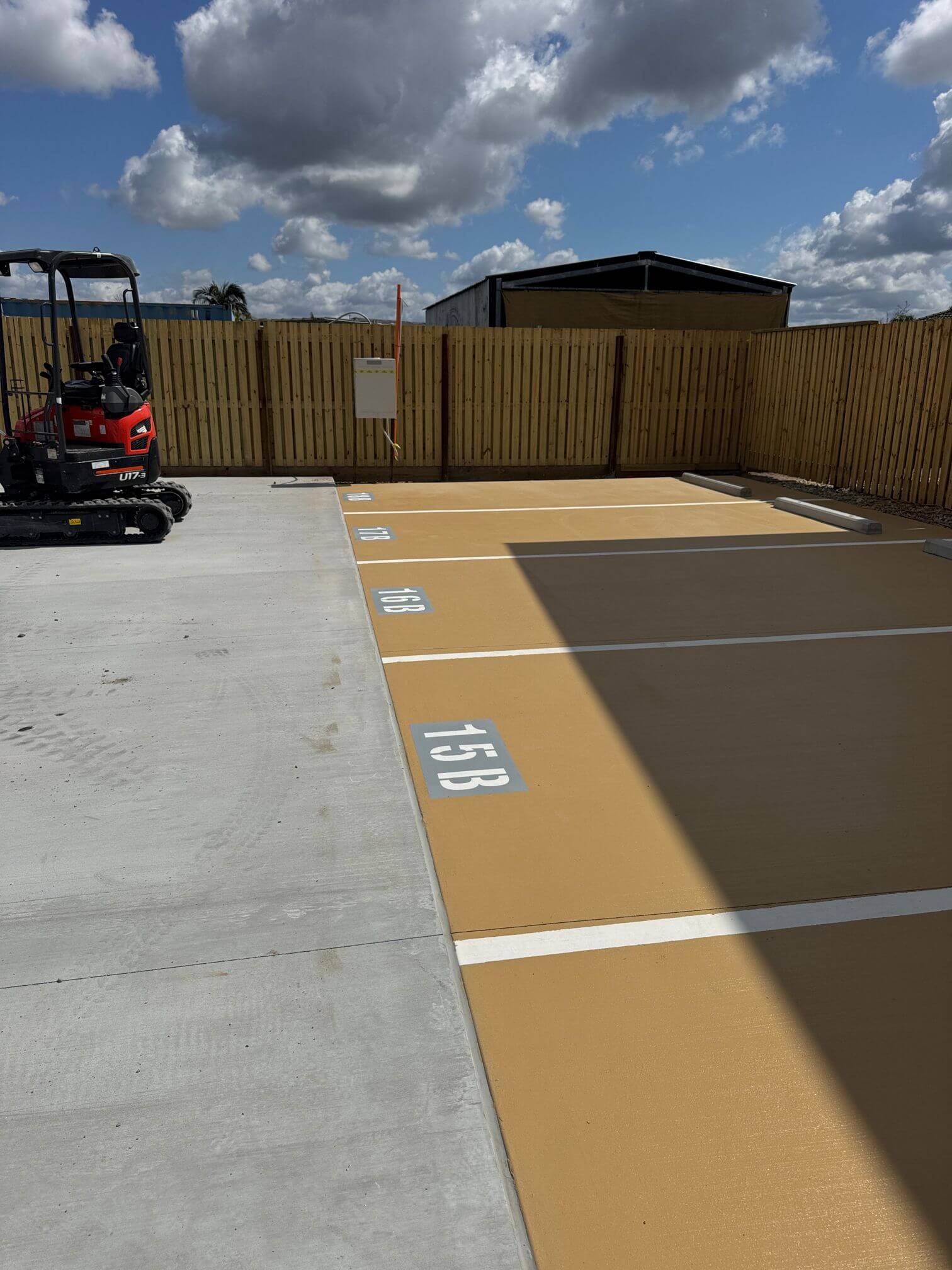 Residential car park in North Brisbane with freshly painted ochre parking bays, white line marking, stencilled bay numbers 15B to 18B and concrete wheel stops