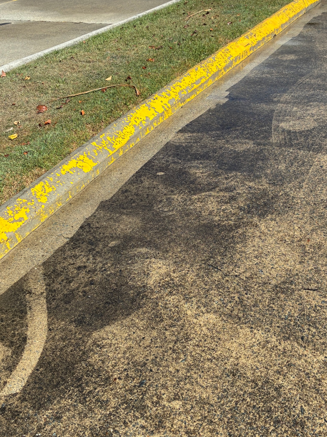 Pressure cleaned asphalt strip beside worn yellow kerb line