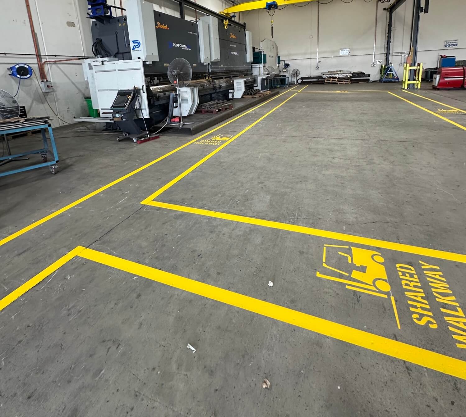 Factory floor with yellow shared walkway line marking and forklift stencils