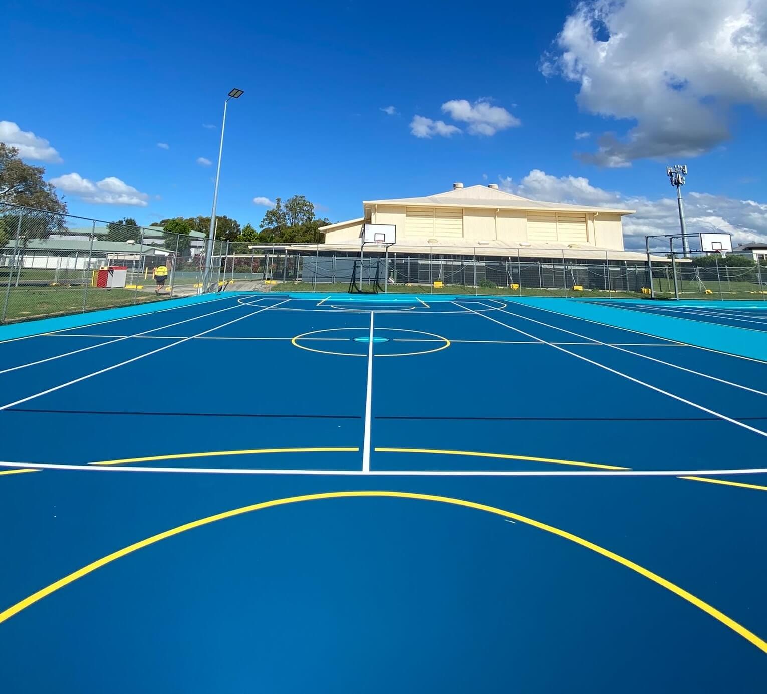 Blue outdoor sports court with yellow and white multi-sport line marking