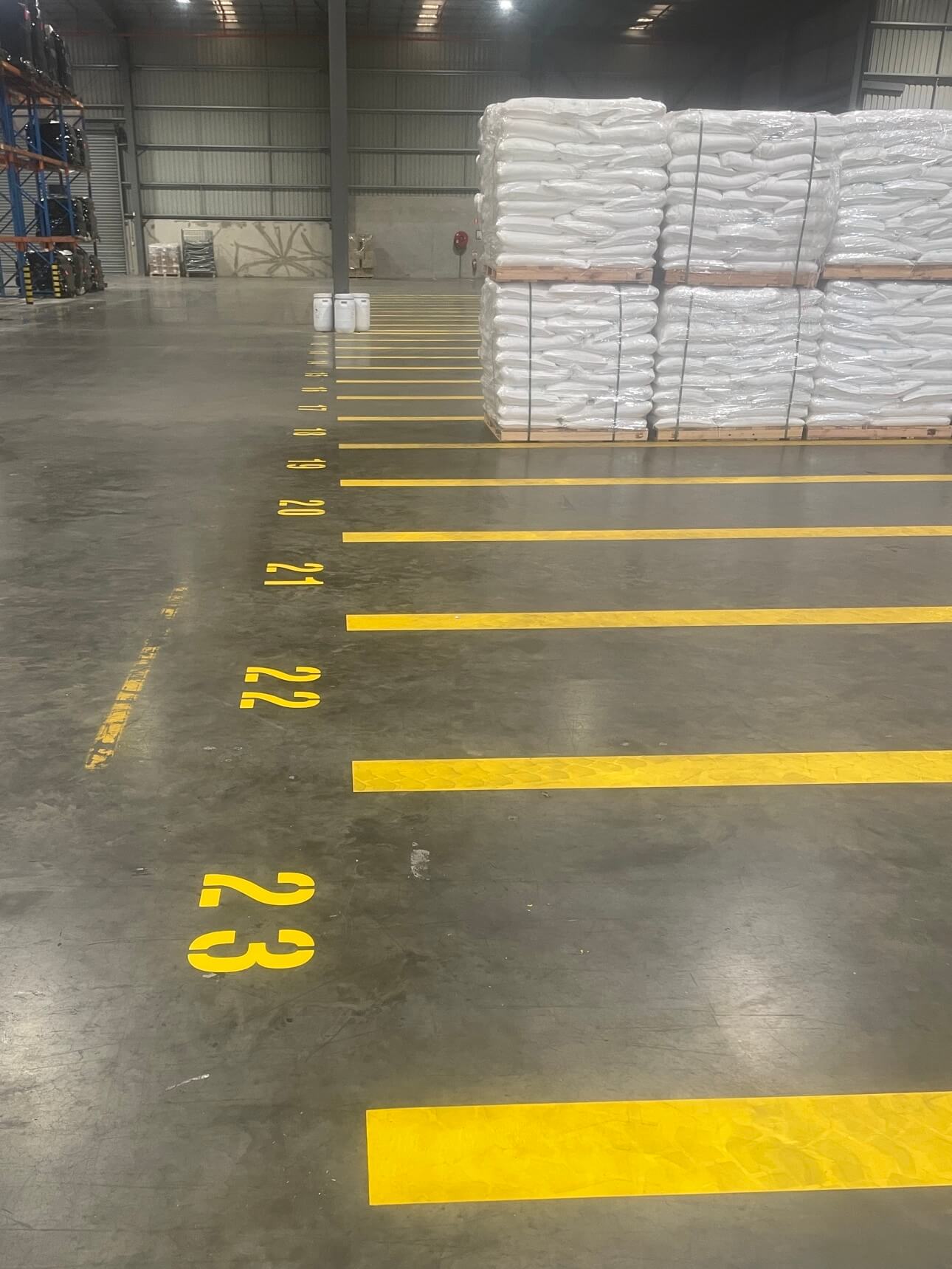 Warehouse floor with numbered yellow pallet bays beside stacked stock