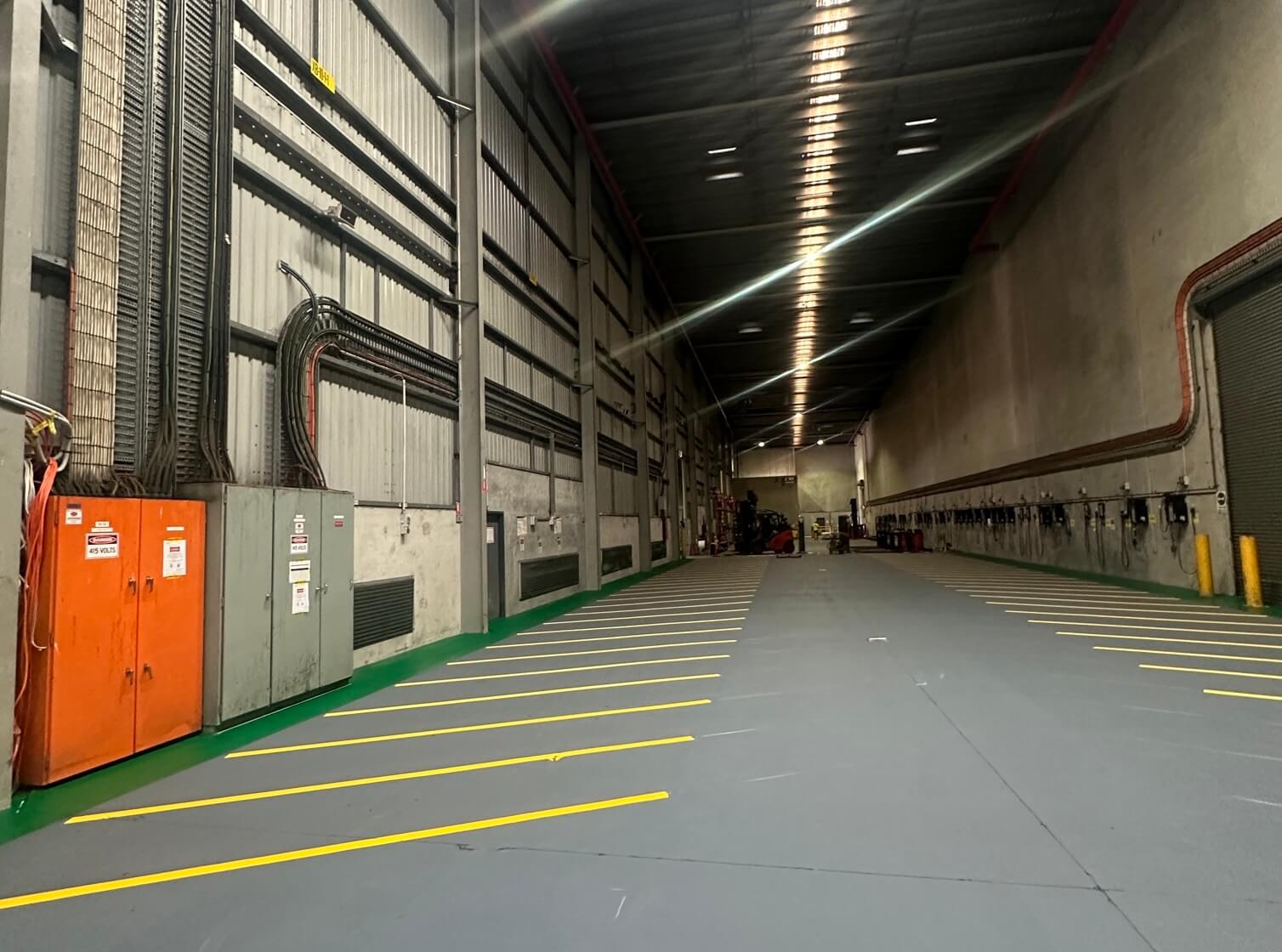Large warehouse with yellow line marked forklift charging bays along the wall