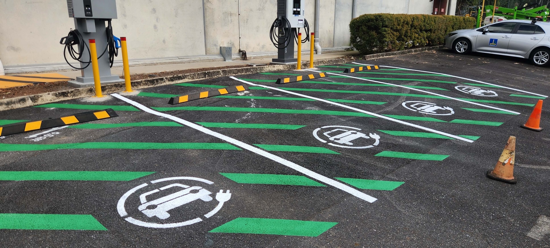 Commercial EV charging bays with green hatching, stencils and wheel stops